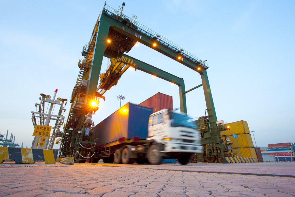 Blurred motion of truck with cargo containers and cranes in a shipping port